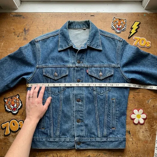 Hand measuring patch placement on a denim jacket with several chenille patches laid out nearby
