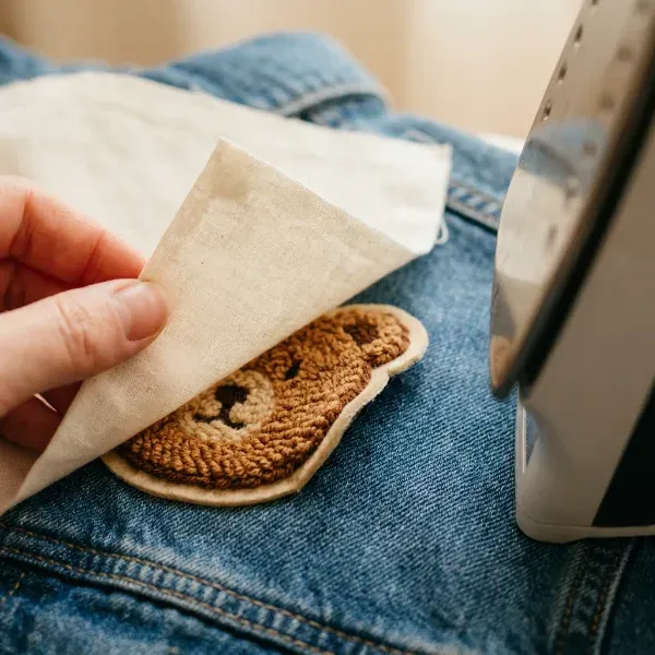 Hand lifting a protective cloth off a chenille patch to check the edges during ironing