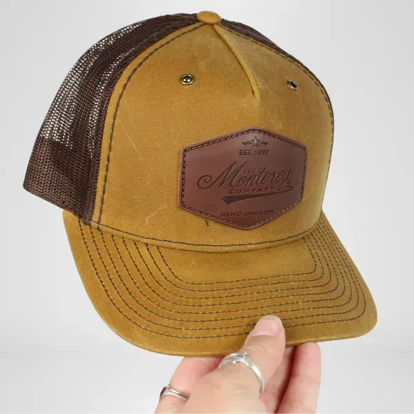 Custom brown trucker hat with embossed leather Monterey patch shown in hand