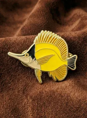 Custom soft enamel lapel pin shaped like a yellow butterflyfish on brown velvet