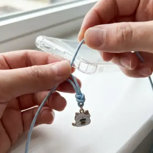 Nylon cord threaded through a phone case lanyard hole with a charm attached