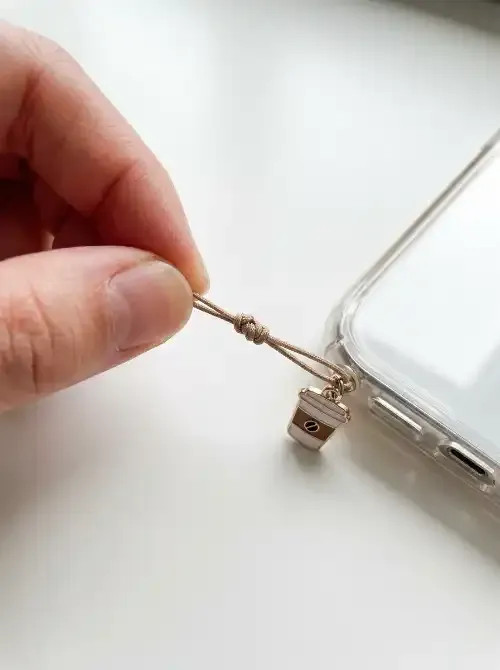 Fingers tugging a phone charm cord to test the attachment before daily use
