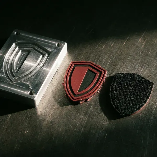 CNC mold plate next to a freshly molded PVC patch and a finished patch showing hook-and-loop backing in a production sequence