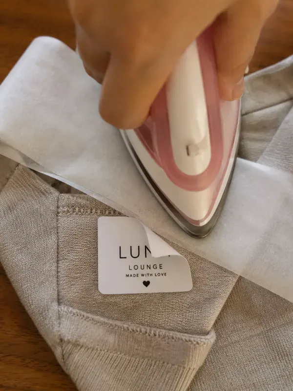Hand lifting a warm iron-on label from fabric with parchment paper underneath