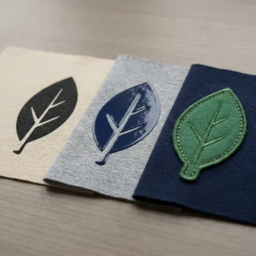 Comparison of screen printed ink, vinyl transfer, and a sewn on patch showing different garment decoration methods